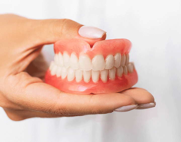 The dentist is holding dentures in his hands. Dental prosthesis in the hands of the doctor close-up. Front view of complete denture. Dentistry conceptual photo. Prosthetic dentistry. False teeth